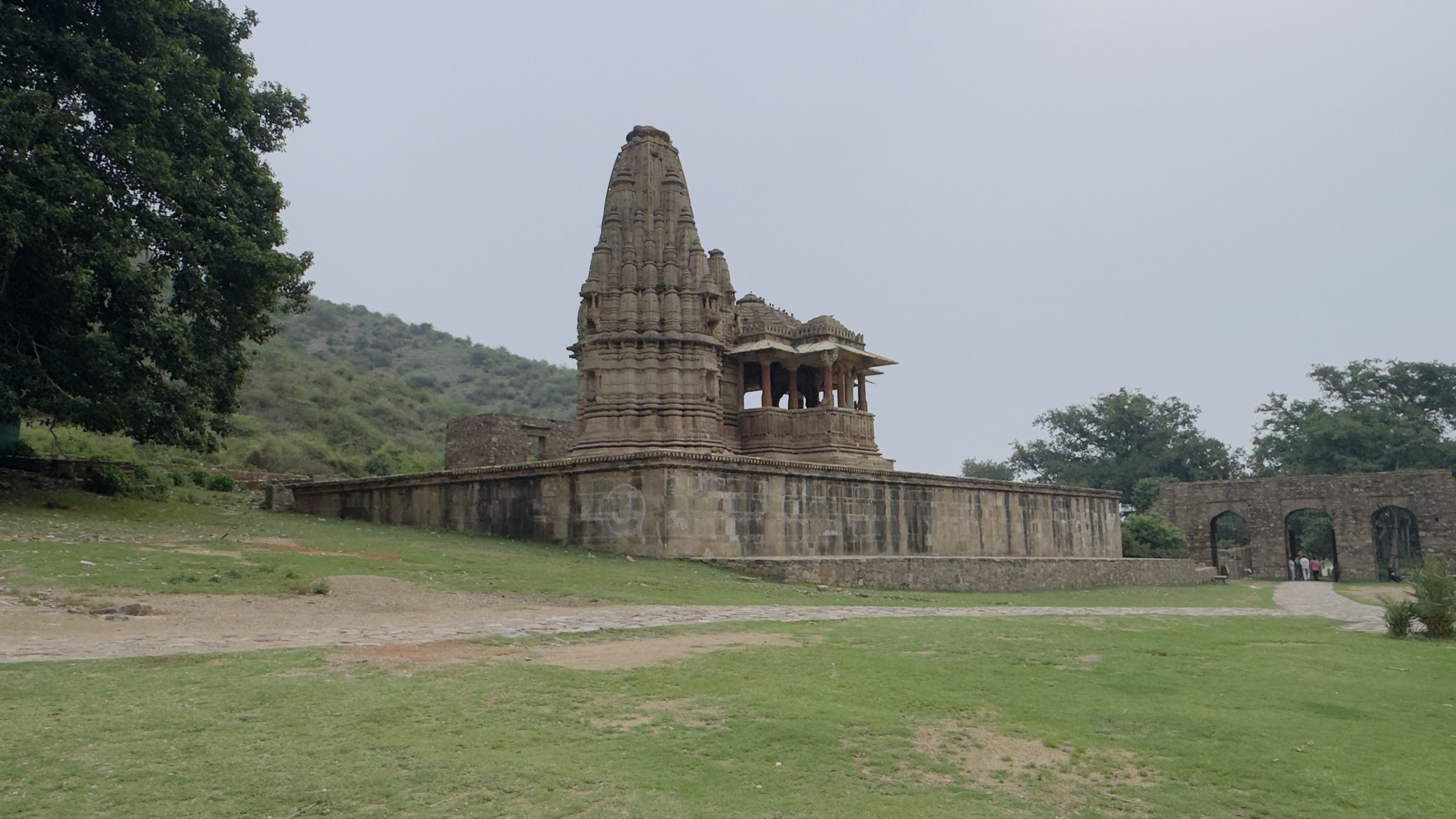 Old stone temple with a carved spire on a raised platform at Bhangarh, an arched gateway to the right